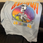 The back of a grey shirt with a skeleton captain and the words Baja Haha 2026. There is a sunset background to the skeleton.